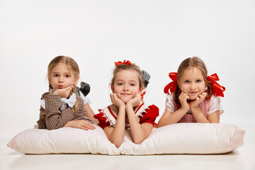 Relaxation and fun. Cute little beautiful girls, kids lying on big pillow against grey studio...