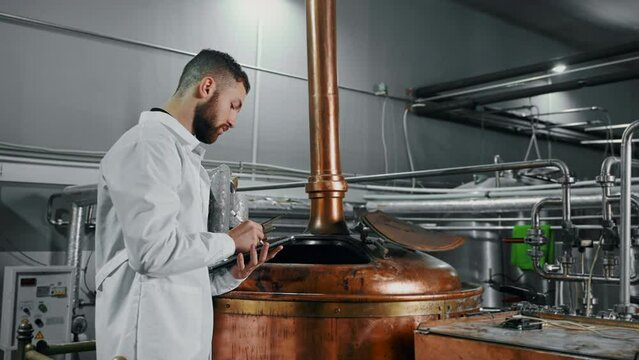 professional technologist in brewery workshop, checking wort in mash kettle tun