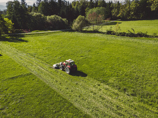 Aerial view of a red tractor mowing a green grass field on a sunny spring day