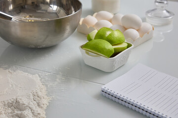 Close-up on the white glossy kitchen table are the ingredients for the festive apple pie. Metal...