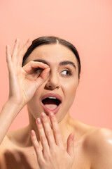 amazed woman covering opened mouth and showing ok sign isolated on pink.