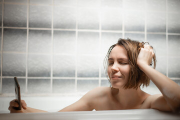 Obraz na płótnie Canvas Sensual middle-aged woman takes a bath and communicates on a mobile phone by video communication. Nude selfie, intimate photo concept. Online dating, love games.