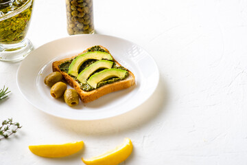 toast with avocado, olives and chimichurri sauce on a white plate. Healthy vegetarian food. White background.