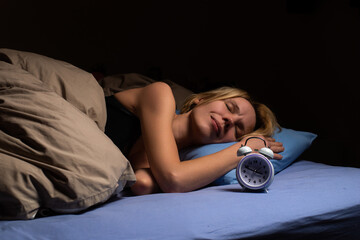 A woman sleeps in bed, there is an alarm clock nearby. Healthy sleep, sleep rest, circadian rhythm...