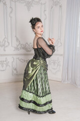 Beautiful woman wearing green medieval vintage Victorian Style dress stand and turn in the room