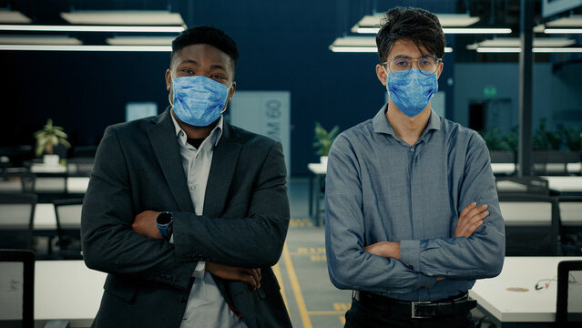 Business people two confident colleagues office workers african indian ethnic men stand with crossed arms in face medical mask. Covid-19 corporate measures prevent disease grippe coronavirus symptoms - Powered by Adobe