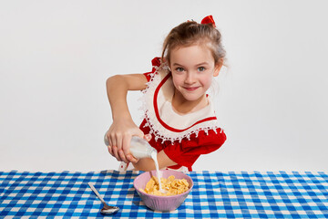 Cute beautiful little girl having yummy healthy breakfast with cereal, posing against grey studio...