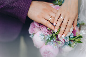 Obraz na płótnie Canvas hands with wedding rings. hands of the bride and groom with wedding rings and bridal bouquet. the groom gently holds the bride's hand