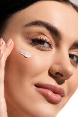 close up view of young woman with face cream on cheek looking at camera.