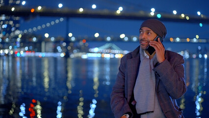 Afro-American man standing at Brooklyn Bridge New York at night - travel photography - obrazy, fototapety, plakaty