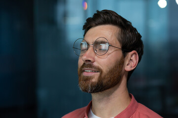 Close-up photo. A young calm man in glasses and a red shirt sits in the office, closes his eyes,...