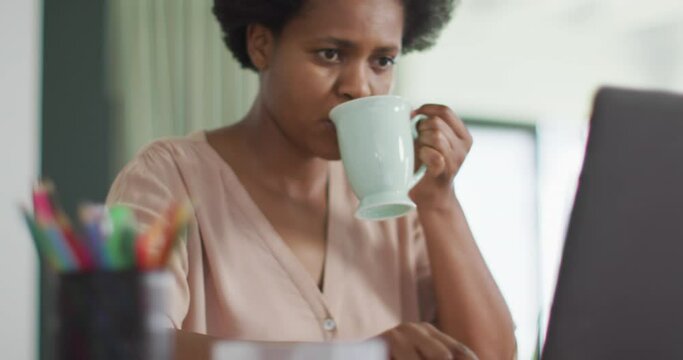 Happy african american woman sitting at table using laptop and drinking coffee