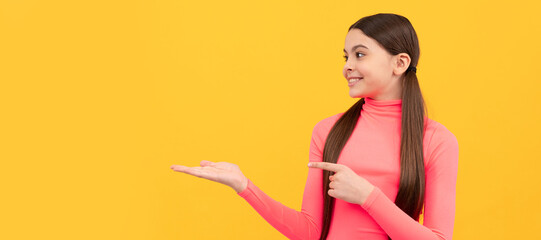 happy child pointing finger on copy space on yellow background, offer. Child face, horizontal poster, teenager girl isolated portrait, banner with copy space.