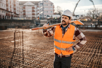 A site worker is holding shovel on shoulder and resting form hard work on reconstruction area. © Dusan Petkovic