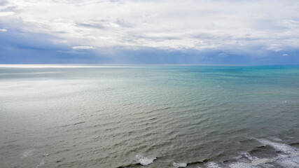 Aerial view of the sea with the horizon. The sky is cloudy and shades of blue color the sea water.