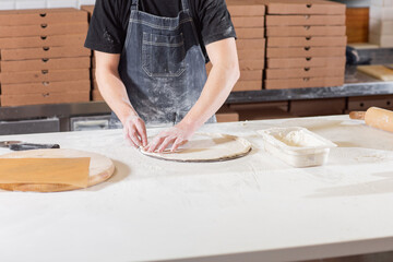 Dough for pizza, the chef rolls out the blanks. Closeup hand of chef baker in uniform white apron cook pizza at kitchen
