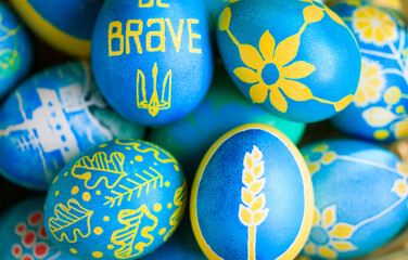 Macro view of Easter eggs painted with Ukrainian national colors, blue and yellow, and depicting Ukrainian national symbols: spikelet of wheat, sunflower, trident, viburnum