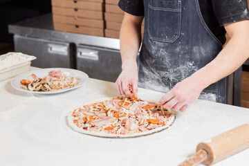 Cooking pizza. Lays out the cheese and salami filling, ingredients on the dough preform. Closeup hand of chef baker in uniform white apron cook at kitchen