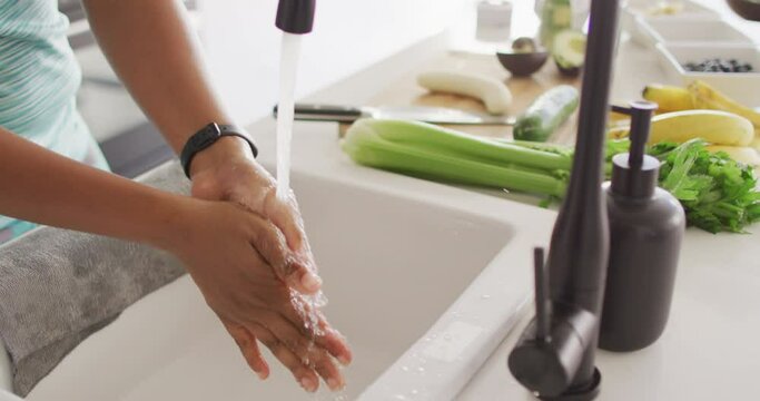 Midsection of african american woman washing hands in sink in kitchen