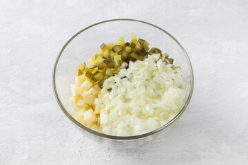 Glass bowl with diced apples, salted cucumbers and onion on a light gray background. Cooking delicious homemade food step by step cooking polish salad