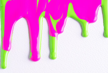 Pink and green liquid drops of paint color flow down on white canvas. Abstract art. Colorful paint dripping on the white wall with copy space.