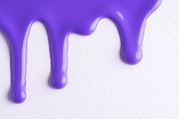 Violet liquid drops of paint color flow down on white canvas. Abstract art. Lilac paint dripping on the white wall with copy space.