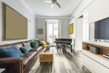 Furnished apartment with three-seater brown leather sofa, white sideboard with tv, black grand piano and balcony with white doors