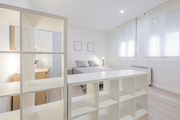 Fototapeta na wymiar Loft apartment with empty white wooden shelves, bedroom with a double bed with gray bedspread and aluminum windows with roller blinds