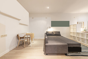 Loft apartment with empty white wooden bookshelves, a three-seater sofa with an extended cmaa and a wooden folding dining table