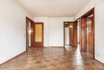 Living room of an empty apartment with cheap dark woodwork, white gotelet walls and brown tiled floors