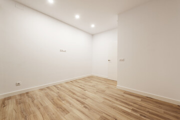 Empty loft with white moldings on doors and skirting boards, smooth white walls and light wooden floors, white aluminum radiators