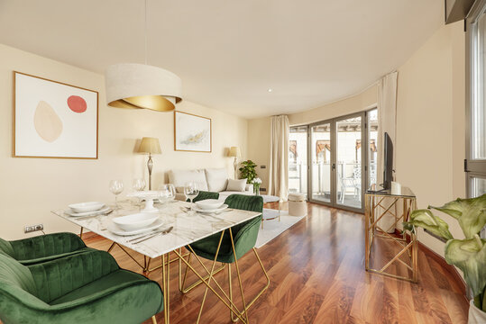 Dining room of a vacation rental home with a white marble dining table and gold metal legs, reddish wooden floors and a terrace with aluminum and glass doors