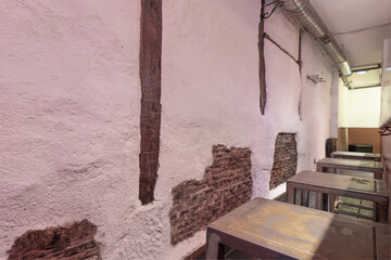 Elongated hall of an empty restaurant with industrial-style metal tables, walls with asymmetric plastering and exposed bricks and wooden beams