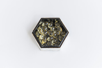 A hexagonal mother-of-pearl box with a black interior filled with pearls of a supreme liquid diet on a smooth white surface