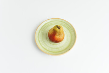 A lone ripe pear on a green plate viewed from above on a smooth white surface