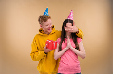 a man gives a birthday present to his girlfriend, making her a surprise isolated over beige background