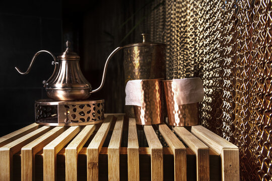 A Metal Tea Set On An Unvarnished Wooden Table With A Chain Curtain Next To It