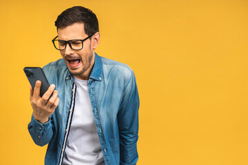 Young caucasian man angry, frustrated and furious with his mobile phone, angry with customer service. Isolated over yellow background. - 577131772
