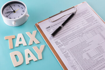 Tax fill concept - 'Tax day' word, clock, pen and calculator  with 1040 U.S. form on blue or green backgound color