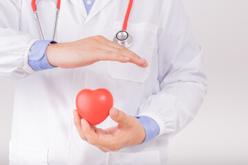 Doctor wear white lab coat with red stethoscope and holding red heart in hands and protect it by another hand. Cardiology healthcare, healthy heart protection, cardiac diseases concept
