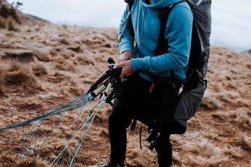 A man prepares his paragliding equipment to fly. A man prepares to jump on a paraglider