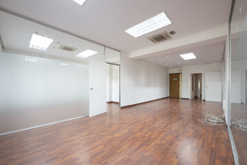 An empty office office with dark wooden floors, technical ceilings and tempered glass partitions