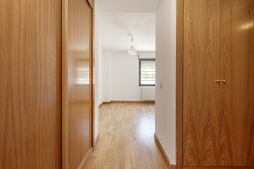 Hallway with a walk-in wardrobe with wooden doors and laminated oak floors and smooth white walls