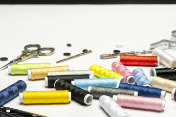 Still life with various coils of colored thread on a white surface, scissors, buttons and other accessories