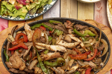 A tray of Mexican chicken and beef fajitas with red and green peppers and white onion