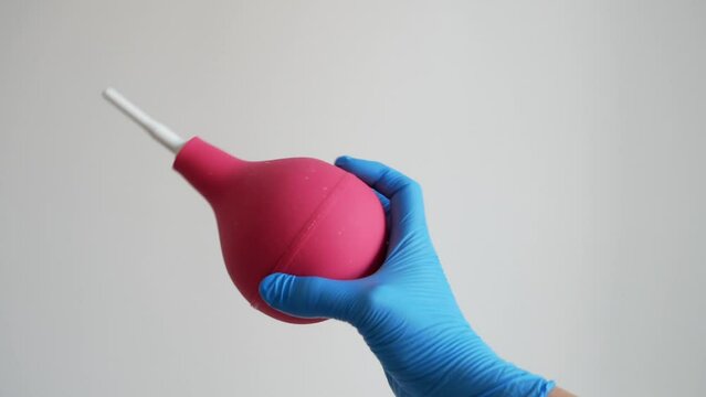 Doctor in blue medical gloves holding red enema isolated on white background, concept