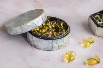 Open mother-of-pearl pillboxes containing vitamin supplement pearls on a reddish marble surface