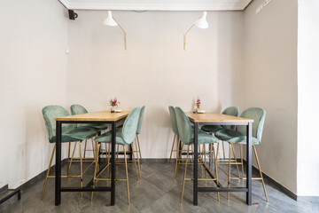 Tall square light wood dining tables with green velvet upholstered stools in a bar diner with lamps and gray tile floors