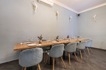 Long light wood dining table with food service set with green velvet upholstered stools in a bar dining room with multi-bulb lamps, light green walls and gray tiled floors