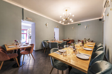 Long light wood dining table with green velvet upholstered stools in a bar dining room with multi bulb lamps and gray tiled flooring